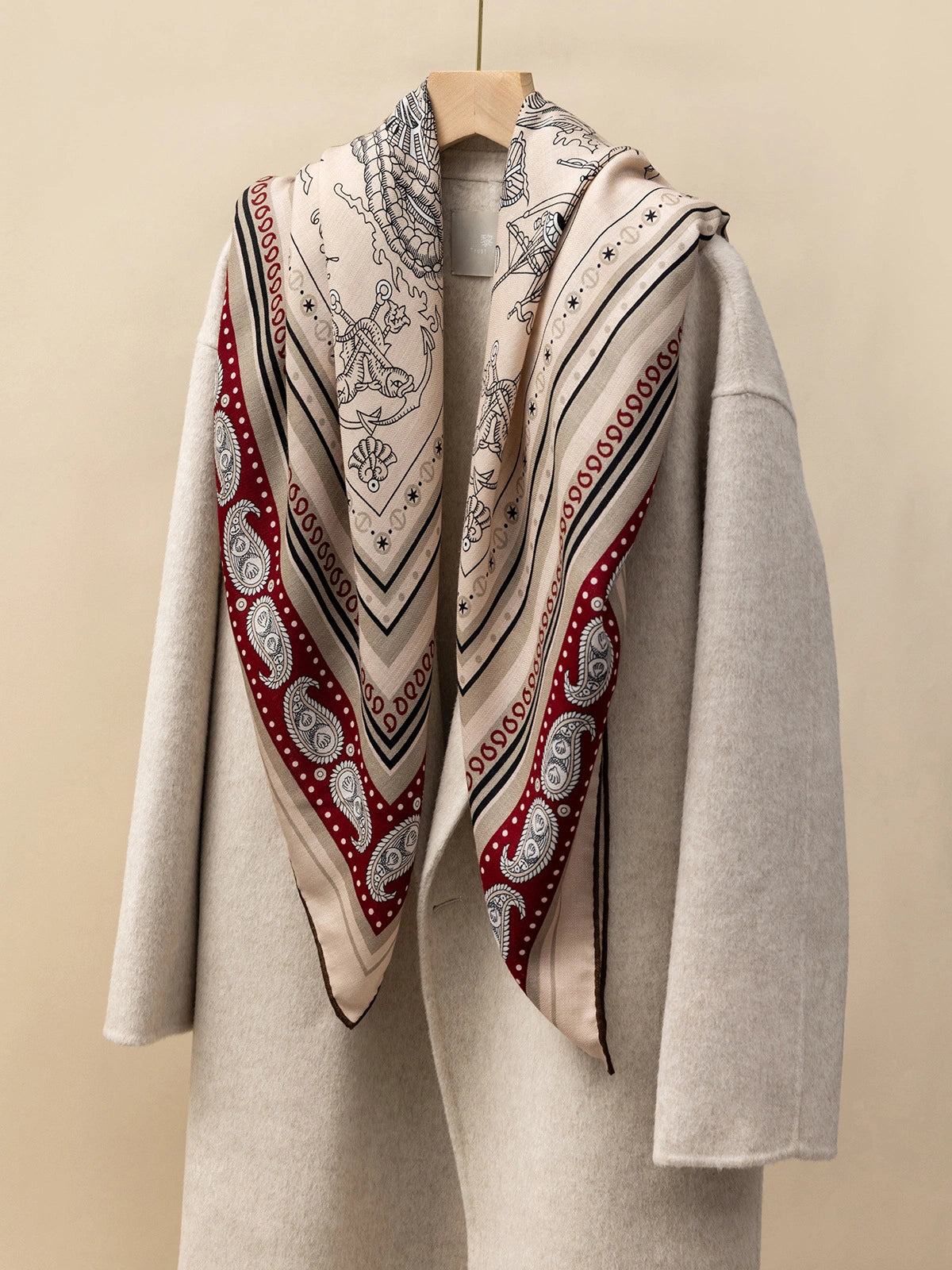 The close-up silk wool square scarf features a nautical fantasy print; draped over a beige coat, it showcases maritime and fantastical motifs.