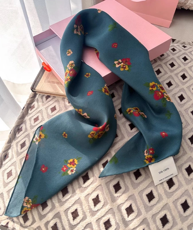 Close-up of greenish-blue floral silk scarf, showcasing the delicate floral pattern and luxurious texture.