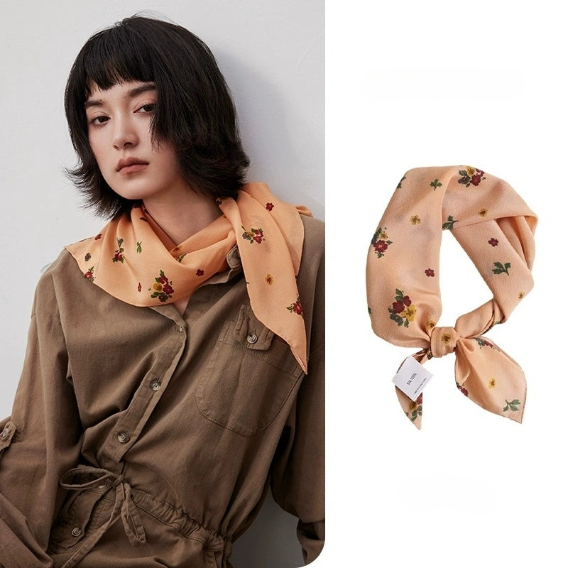 Close-up of light orange floral silk scarf showing its intricate floral pattern and smooth texture.