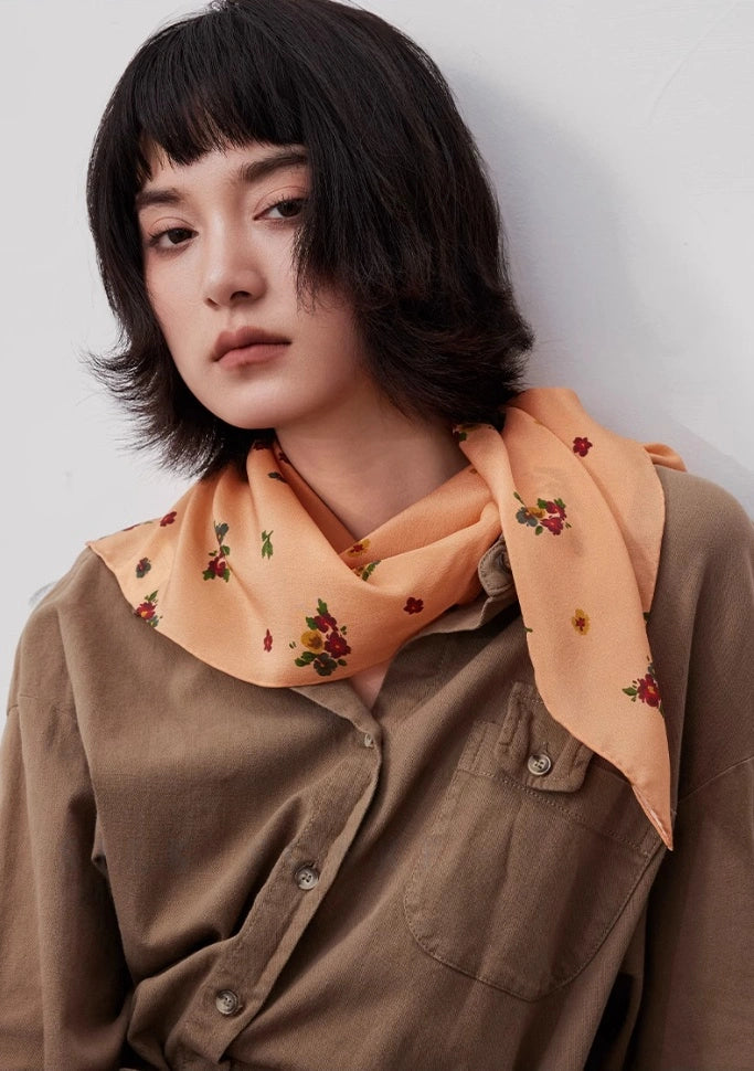 Light orange floral silk square scarf styled as a neck accessory, demonstrating elegance and versatility.