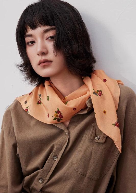 Light orange floral silk square scarf styled as a neck accessory, demonstrating elegance and versatility.