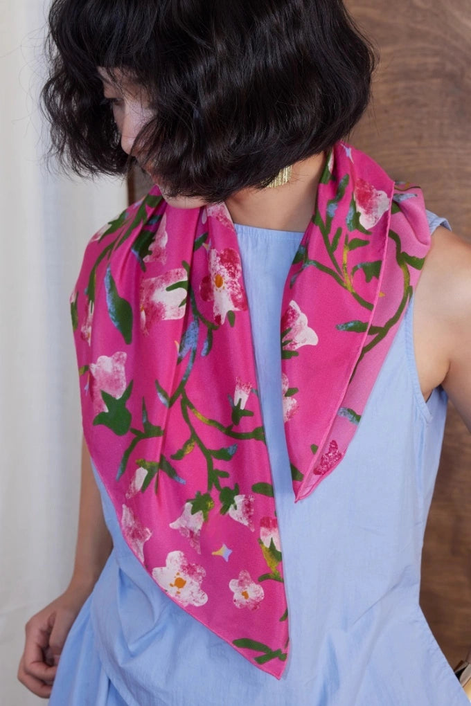 Woman wearing a Berry Powder silk square scarf (63x63cm) as a neck accessory over a blue dress, featuring a floral mulberry silk design.
