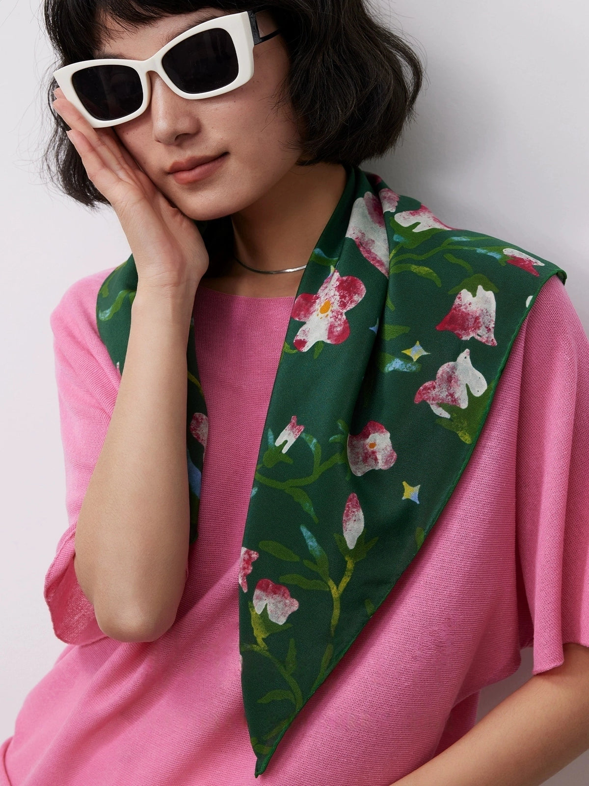 Woman wearing Wilderness Green silk square scarf (63x63cm) as a neck accessory, featuring pink morning glory pattern on mulberry silk, with pink top.