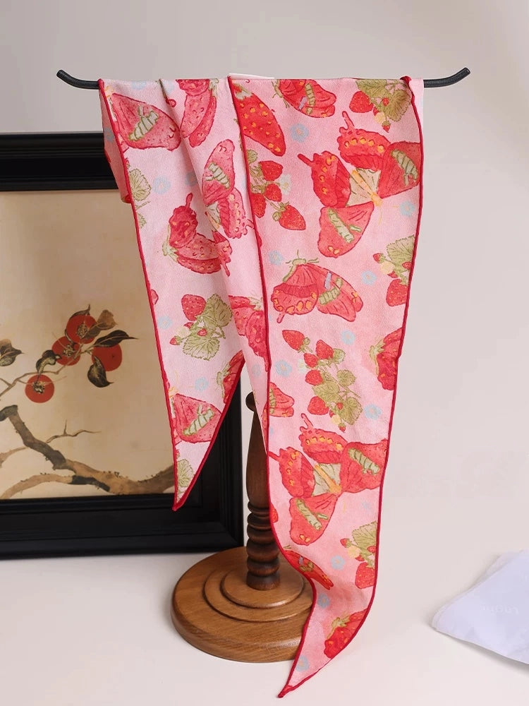 Berry red silk scarf with butterfly print draped near handbag, elegant accessory detail