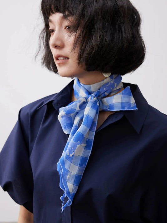 Lightweight blue plaid silk scarf tied at the neck, showcasing its soft mulberry silk georgette texture.