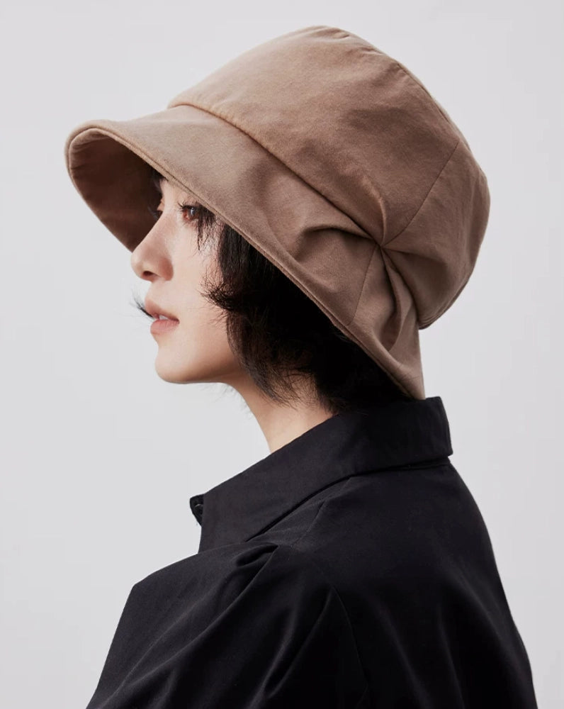 Side profile of a camel pleated bucket hat showing the curved brim and layered pleat detail