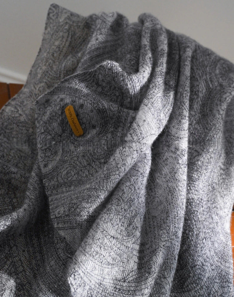 Charcoal grey cashmere scarf in loose folds, highlighting the paisley pattern and fabric texture.