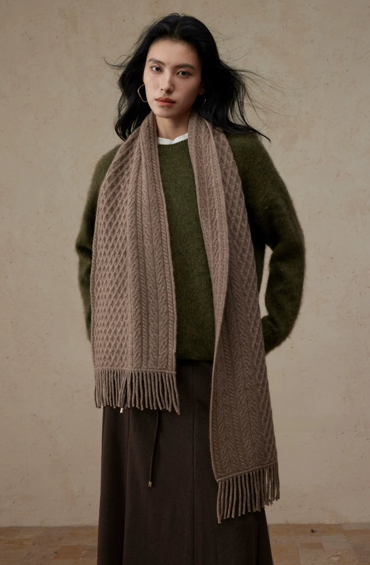 Coffee brown cable knit scarf draped over an olive sweater, with fringed ends hanging at different lengths.