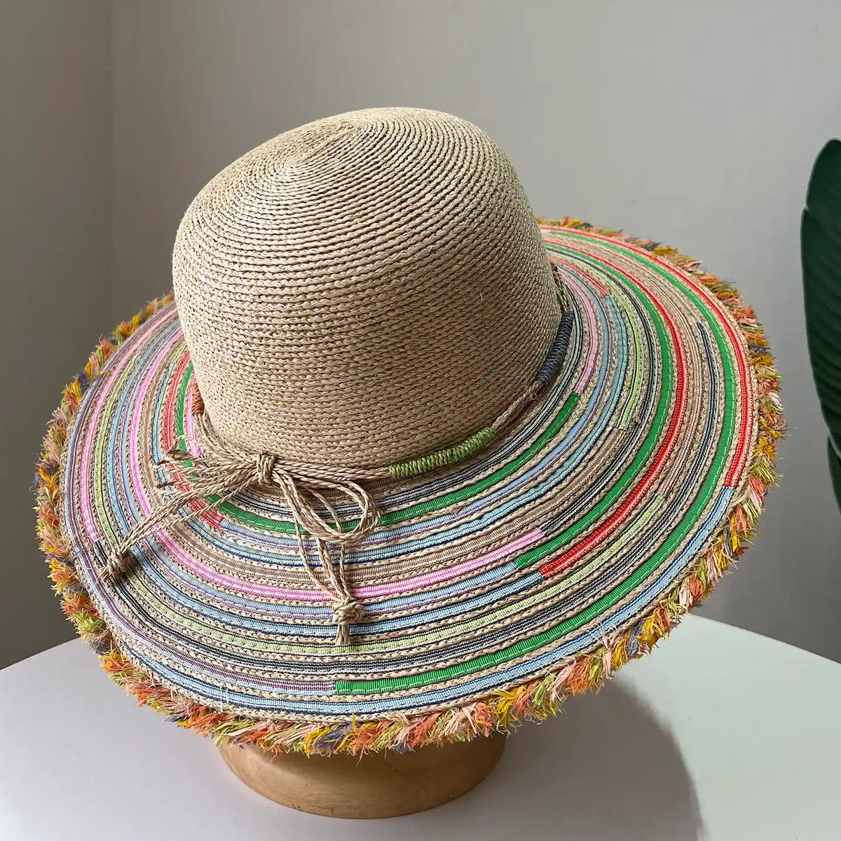 Top view of beige raffia wide brim sun hat with colorful striped brim and frayed edge.