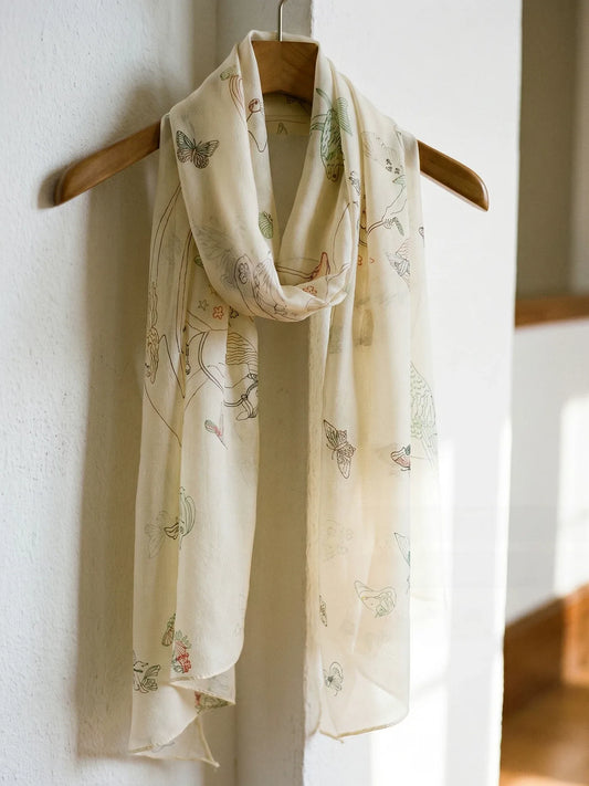 Cream mulberry silk georgette scarf draped over a wooden hanger, showing delicate Pegasus and butterfly motifs.