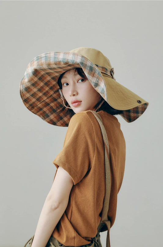 Model wearing khaki and plaid wide brim outdoor sun hat with string, styled for relaxed travel outfits.