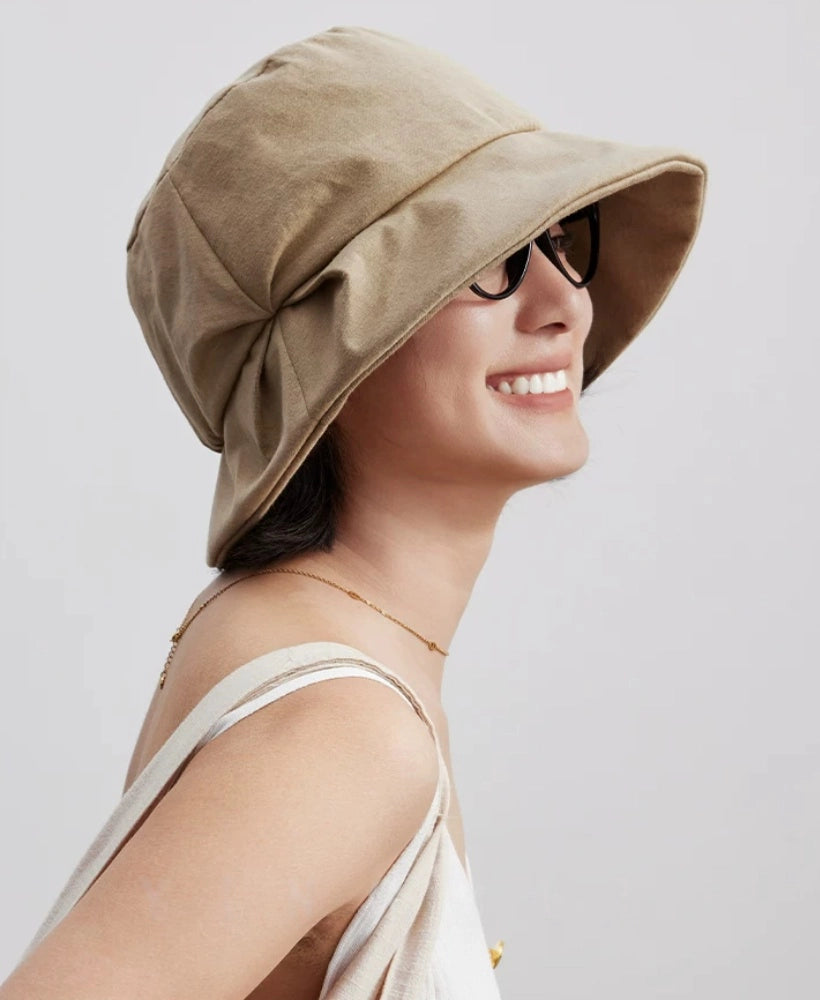 Side view of a light khaki pleated sun hat with a curved brim and sculpted fold detail
