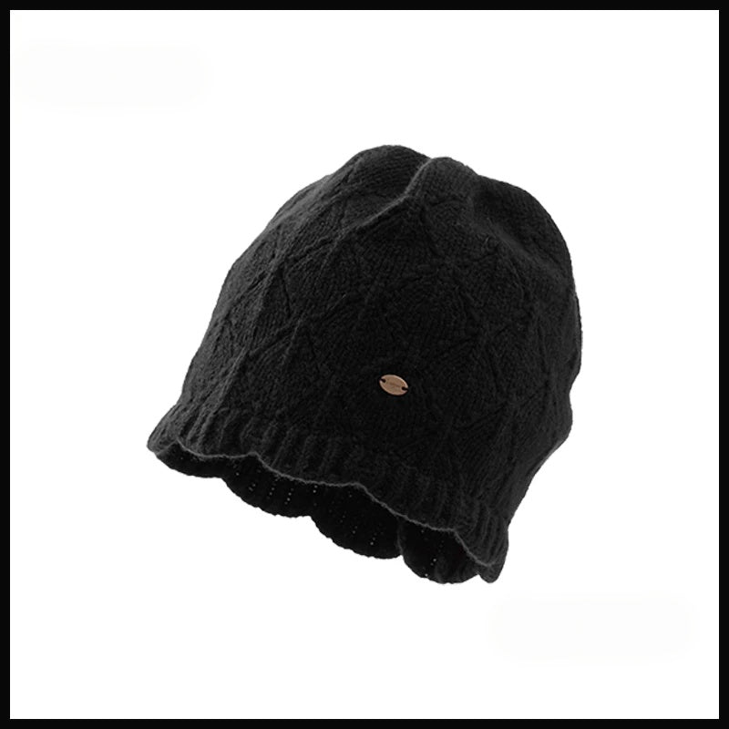 Black wool pointelle knit beanie with a scalloped edge and gold-tone badge on a white background.