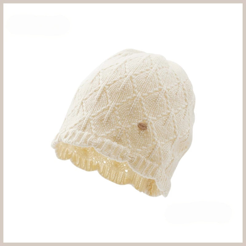Cream-white wool pointelle beanie with diamond openwork, a scalloped edge and a gold-tone badge.