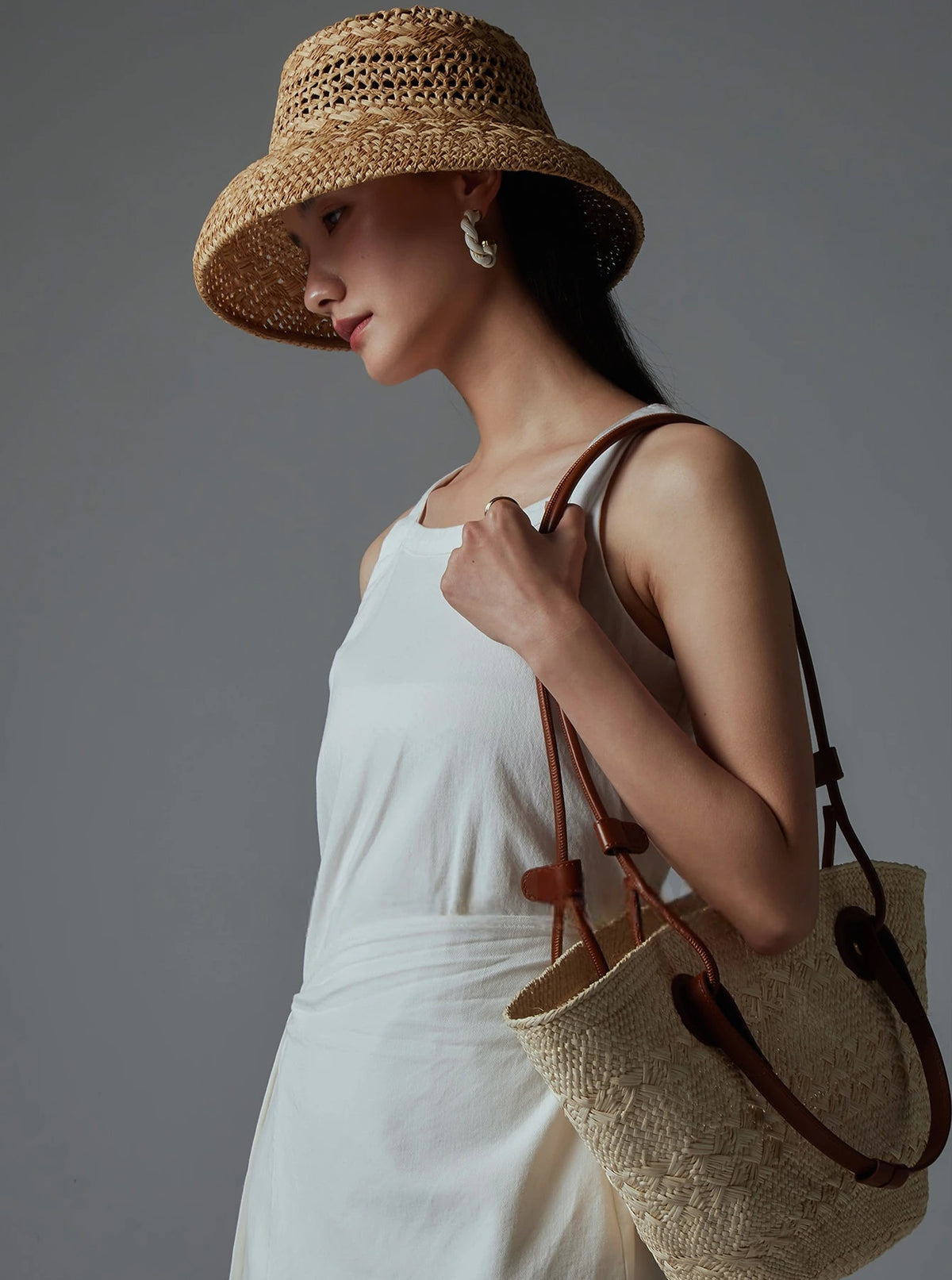 Woman wearing a natural raffia sun hat with a white summer dress and woven bag