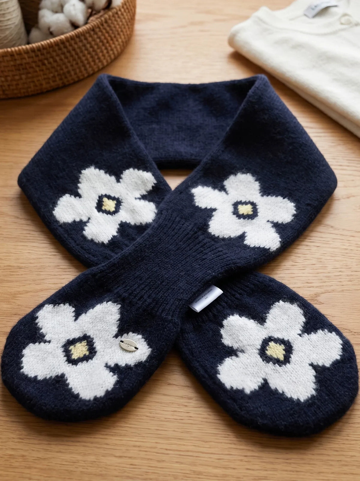 Navy wool keyhole scarf laid flat on a wooden surface, showing white flowers, crossed ends and knit texture.