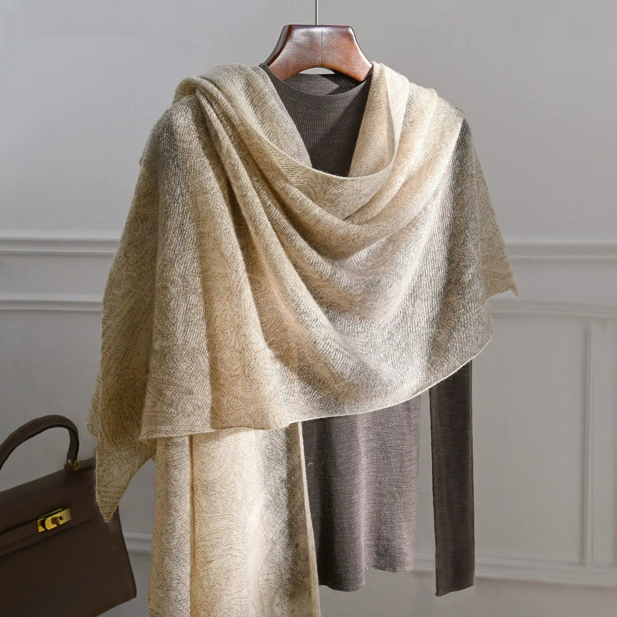 Oatmeal cashmere scarf with a subtle tonal pattern draped across a brown top on a hanger.