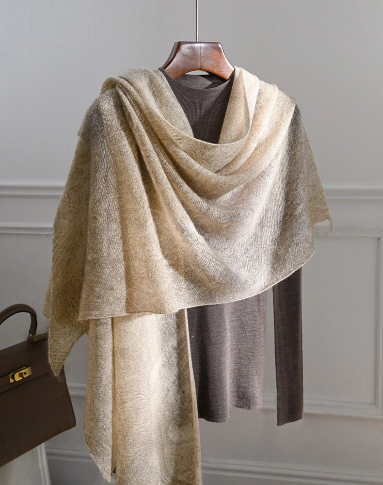 Oatmeal cashmere shawl with an asymmetrical drape and long hanging ends over a brown top.