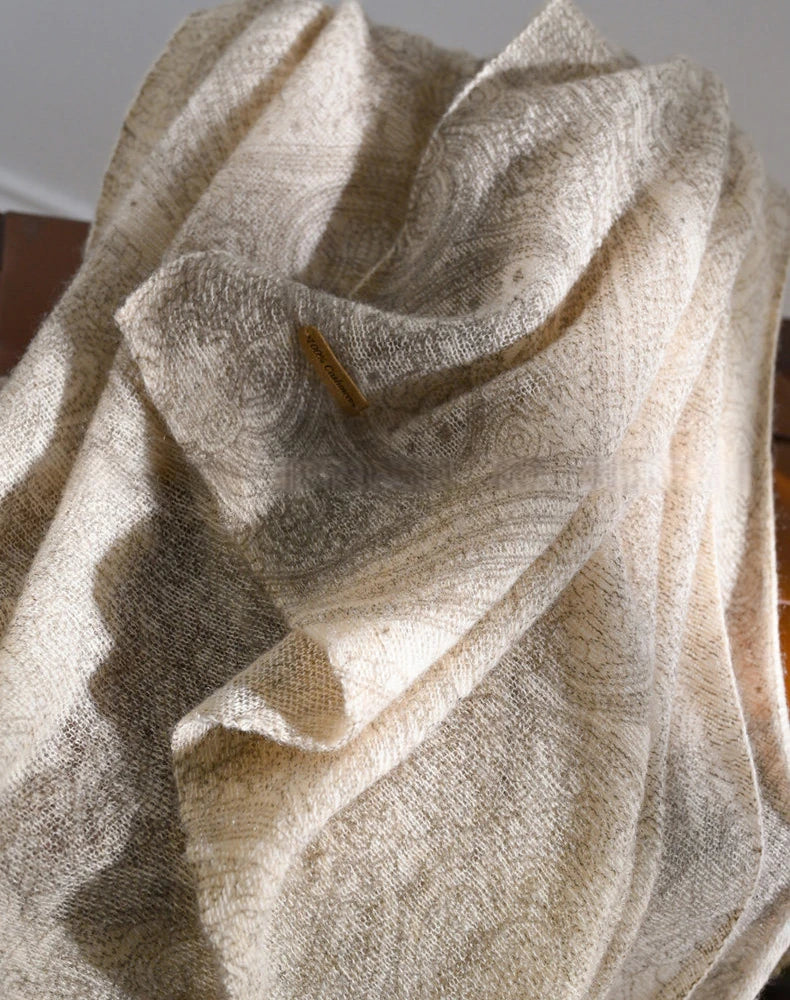 Oatmeal cashmere scarf gathered into soft folds, showing its subtle tonal pattern and fabric texture.