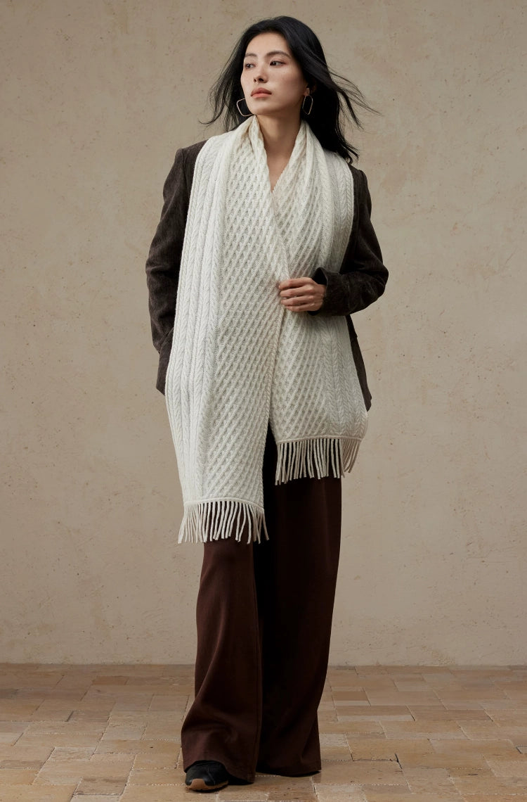 Full-length view of a model wearing a long pure white cable knit scarf with fringed ends over a brown outfit.