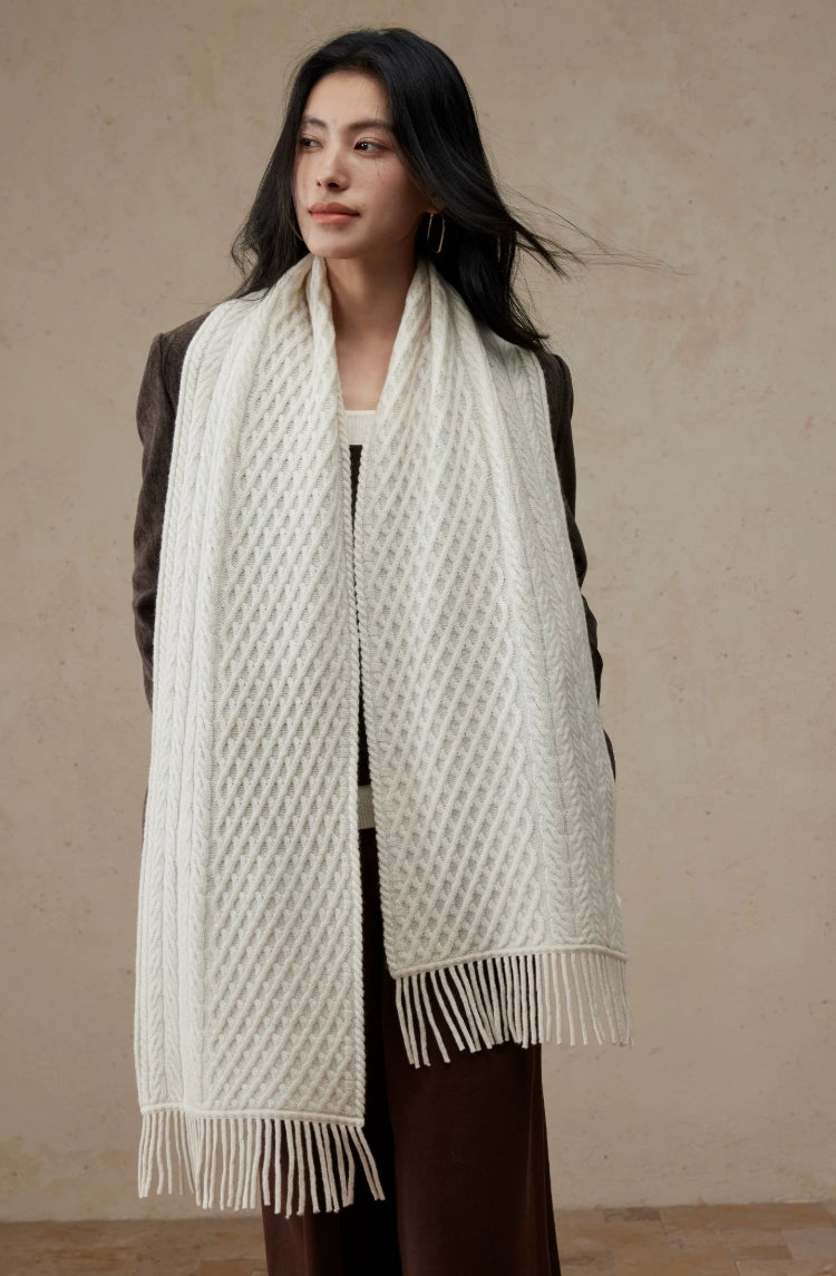Pure white cable knit scarf draped around a model's neck, with long fringed ends hanging down the front.