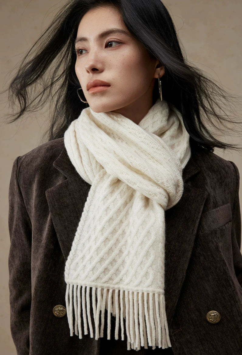 Close-up of a pure white cable knit scarf knotted at the neck, showing its diamond knit pattern and fringe.