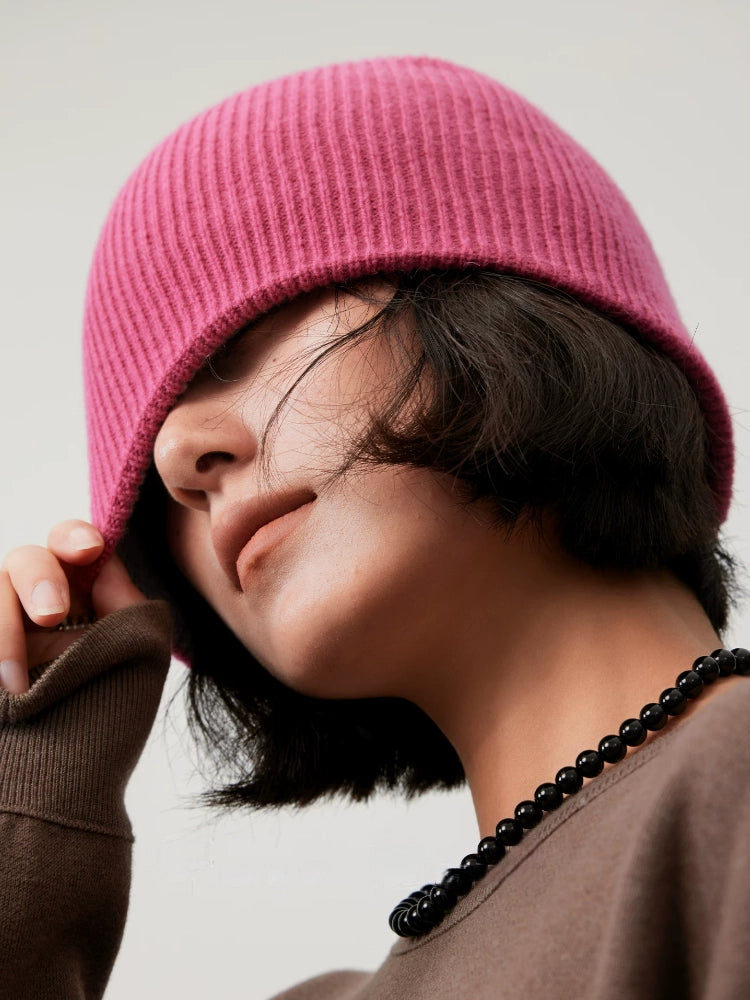 Close-up of a model pulling down the edge of a rose pink rib-knit wool beanie.