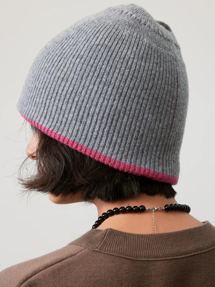 Rear three-quarter view of a light gray wool beanie, showing the ribbed crown and contrasting rose pink edge.