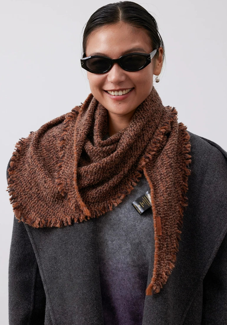 Model wearing a terracotta cashmere triangle scarf loosely around the neck, with a fringed point resting on one shoulder.