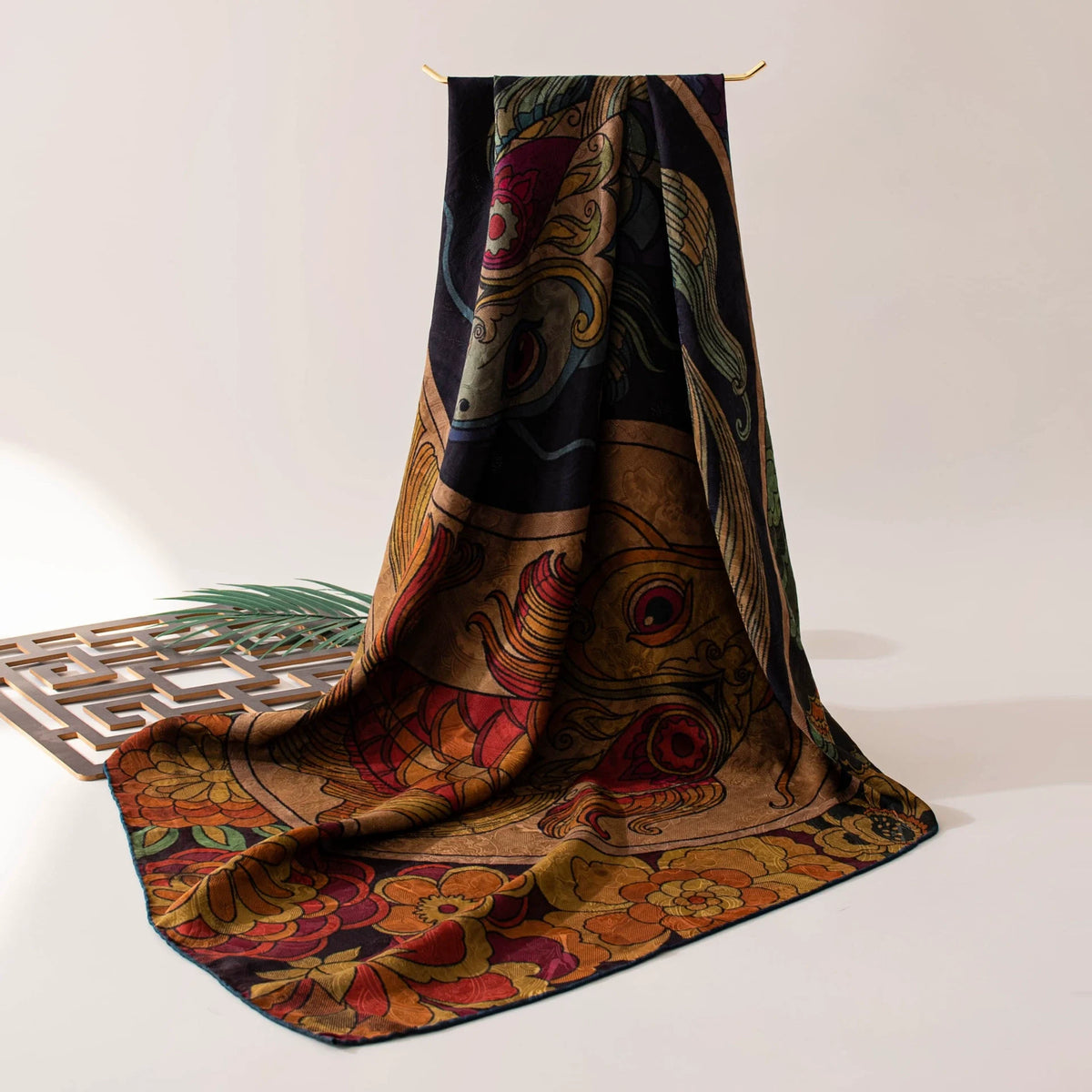 Twin fish Xiangyun silk scarf draped on a table, showing its dark floral border and lustrous finish
