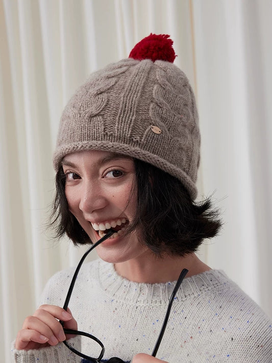 Vintage cable knit wool beanie in oatmeal with a red pom pom, shown on a model.