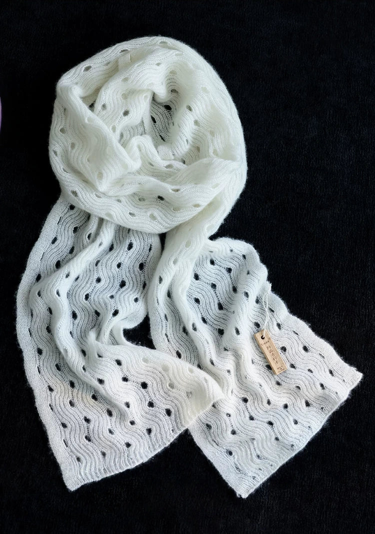 Cream white wave pointelle cashmere scarf loosely coiled on a black background, showing its openwork knit.