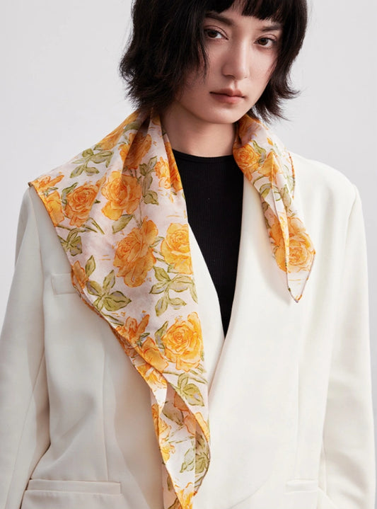 A yellow-rose colored silk square scarf tied at the neck adds a touch of refinement and elegance.