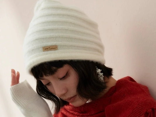 Woman wearing a cream cashmere beanie and a red fringed scarf.