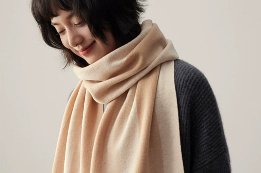Woman wearing a beige scarf loosely wrapped around her neck over a dark gray knit sweater.