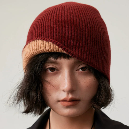 Woman wearing a burgundy rib-knit beanie with beige trim against a light gray background.