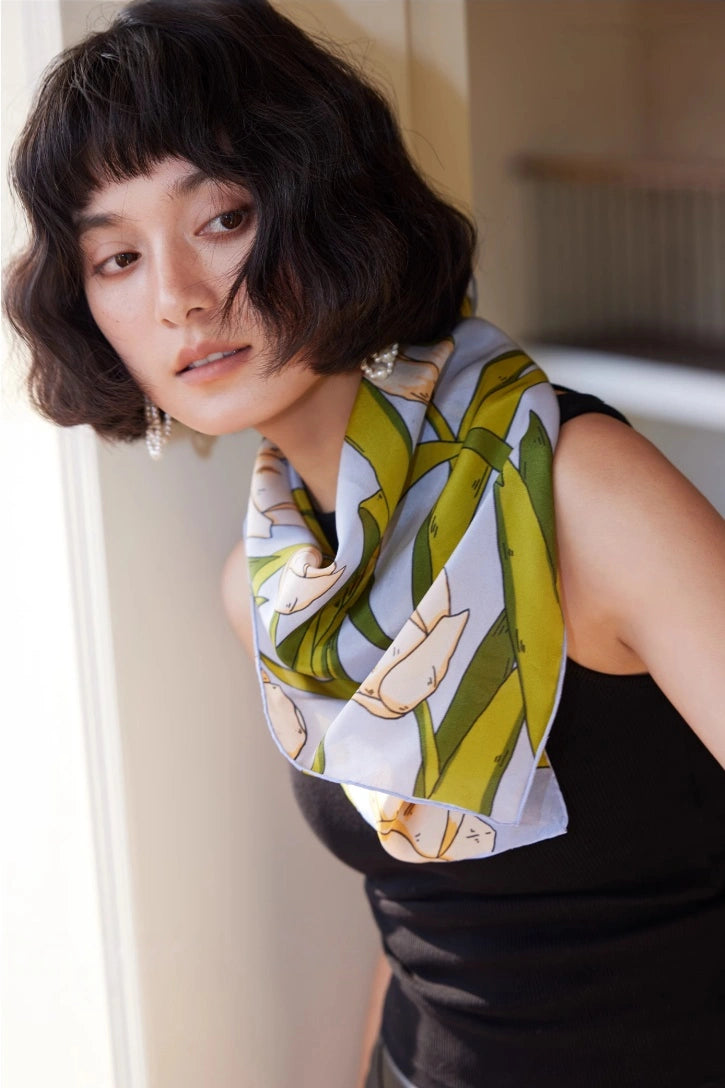 A blue tulip floral print silk square scarf made from 100% mulberry silk is shown close-up as a neck scarf.