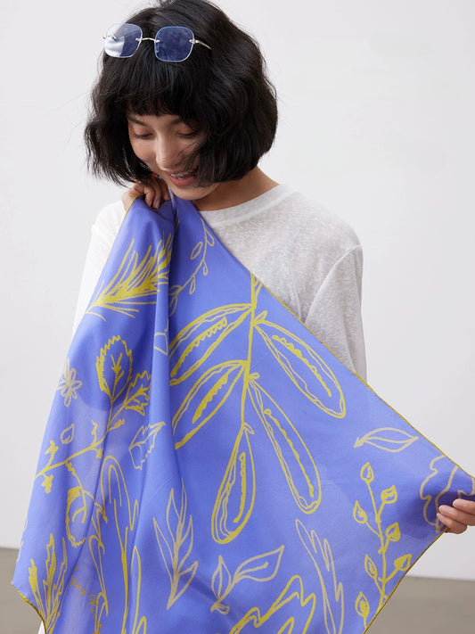 Woman holding a Blue silk square scarf (63x63cm) with yellow botanical print, made of mulberry silk, over a white top.