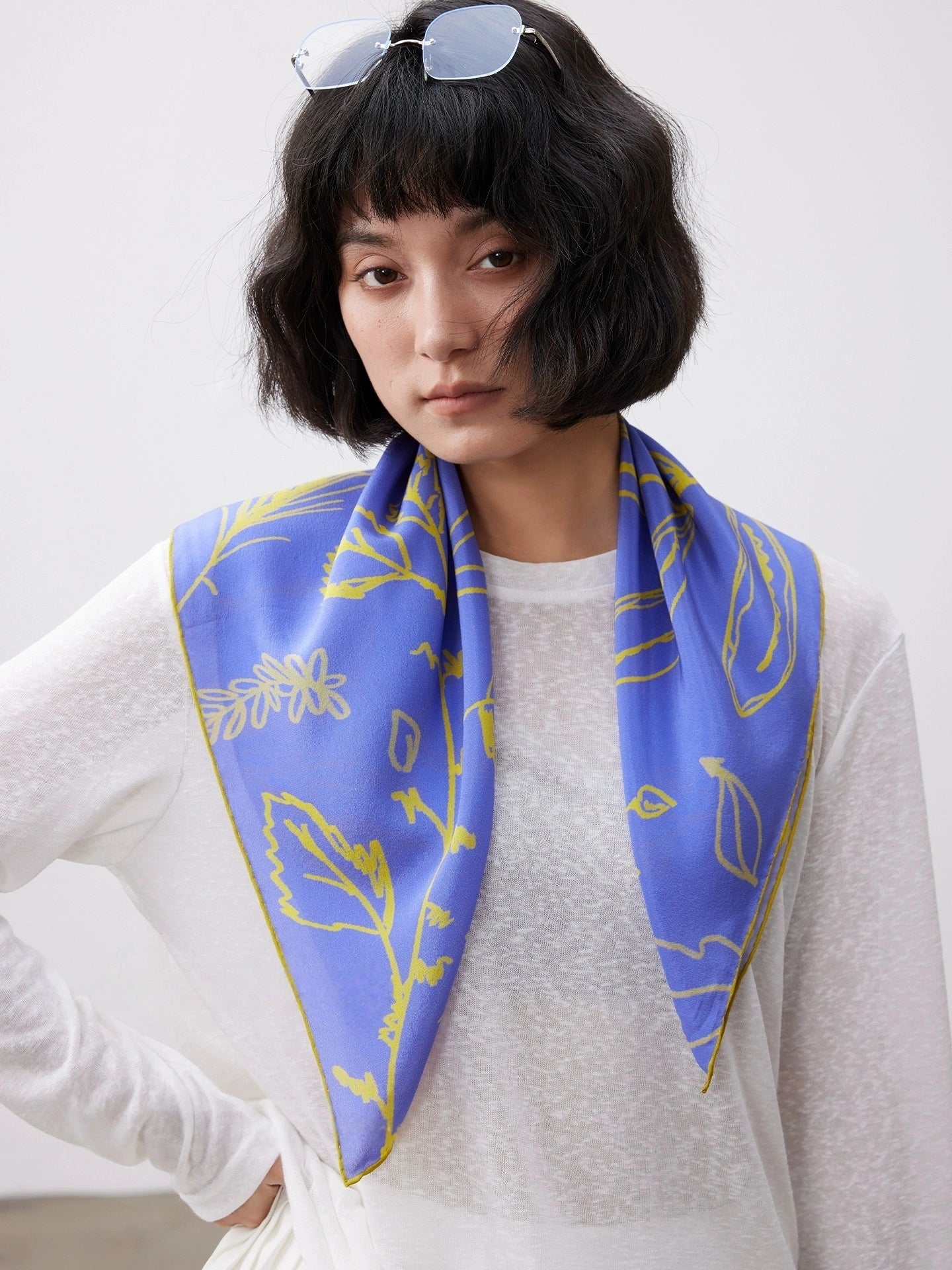 Woman wearing a Blue silk square scarf (63x63cm) with yellow botanical print as a neck accessory, mulberry silk design.