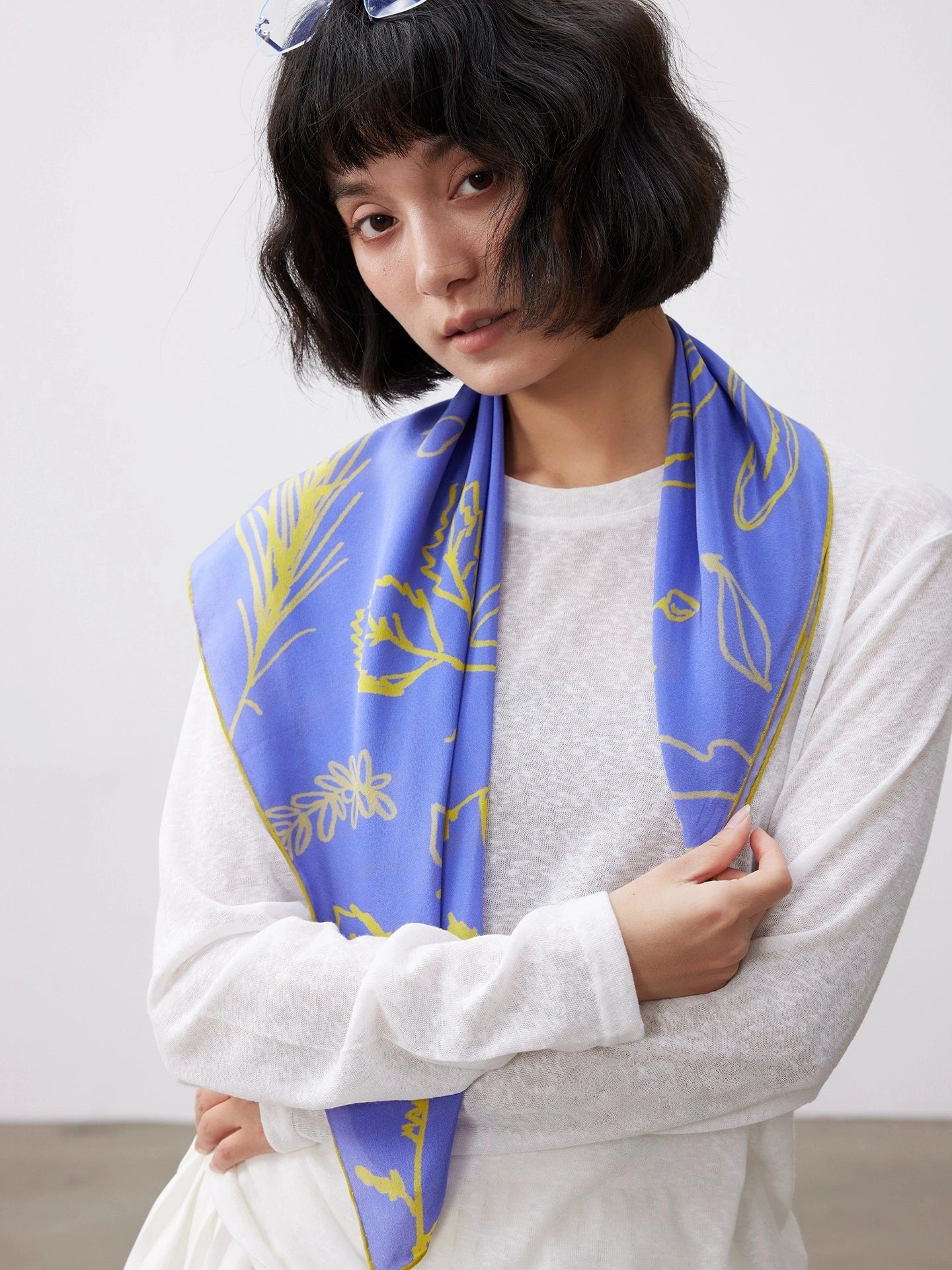 Blue silk square scarf (63x63cm) with yellow botanical print, draped over shoulders, highlighting mulberry silk texture.