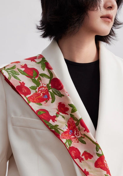 Close-up of blush pink pomegranate butterfly silk scarf styled on a white blazer