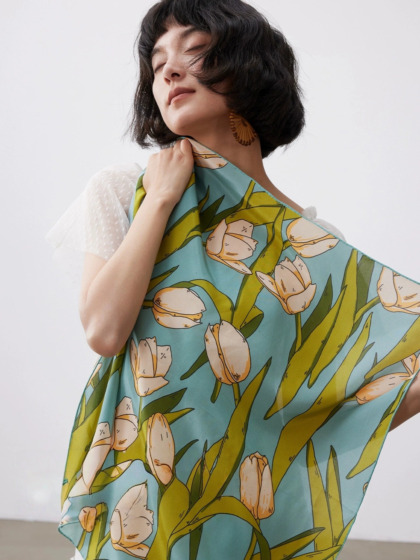 A model displays a close-up of a green tulip floral-print silk scarf.