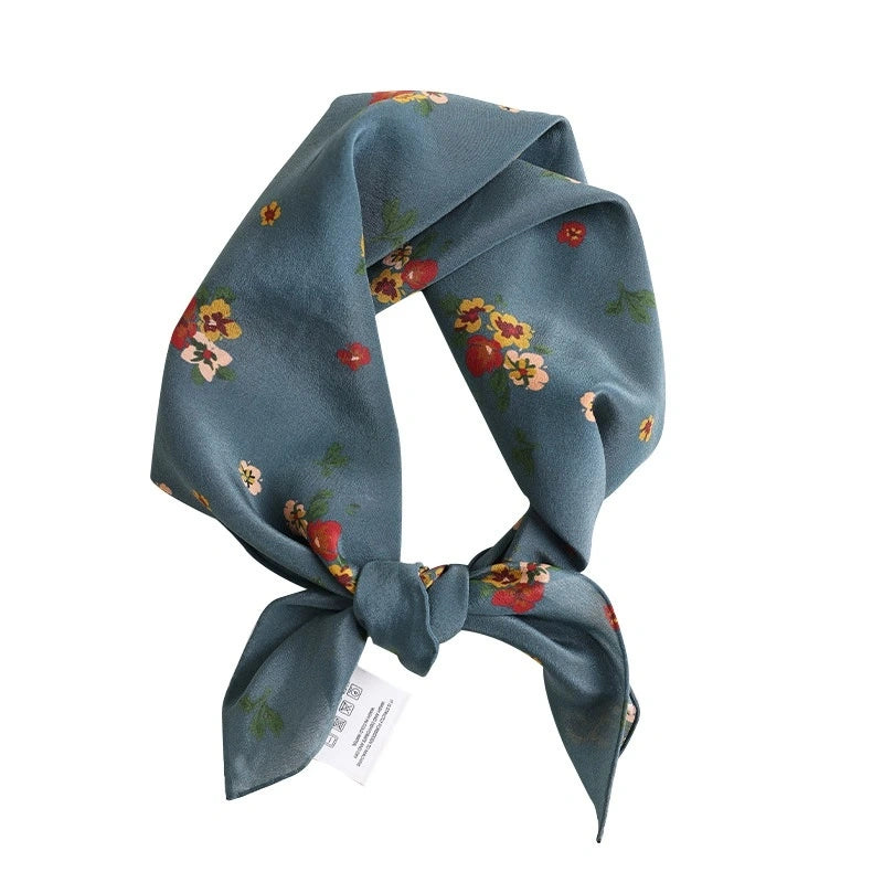 A close-up of a floral-print Greenish-blue silk square scarf highlights the delicate floral pattern and luxurious silk material.