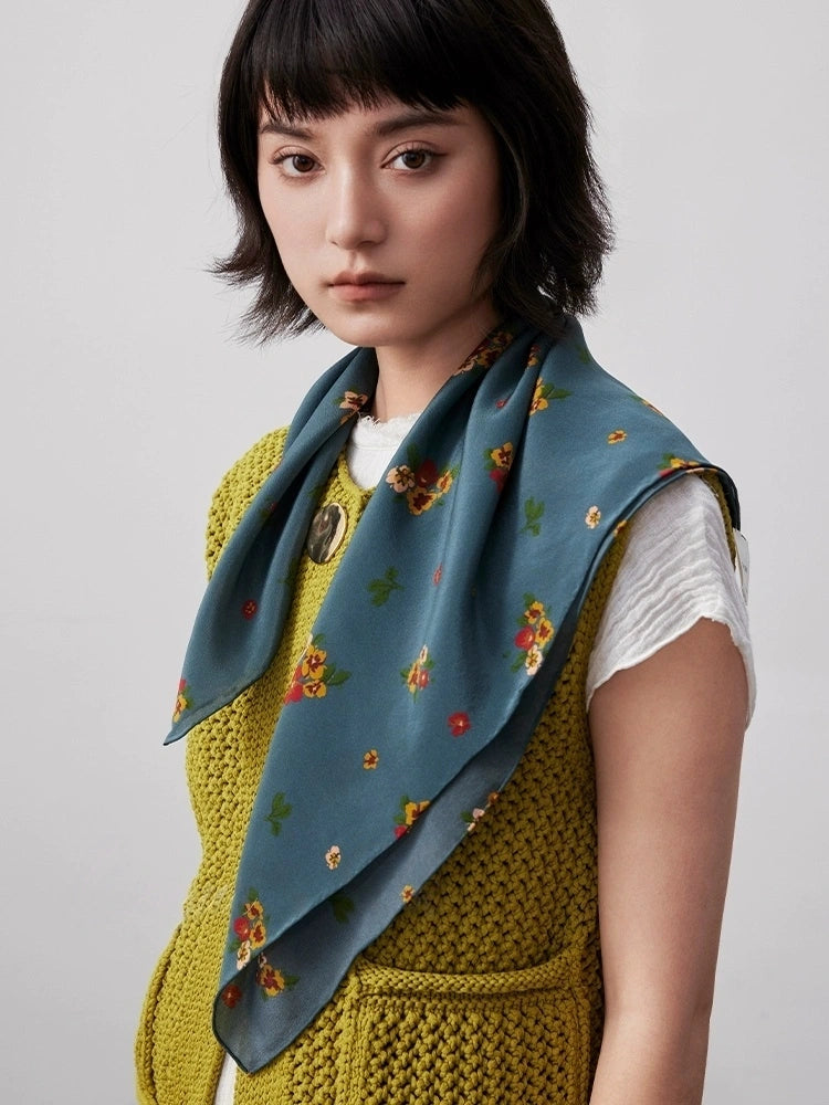 Greenish-blue floral silk square scarf draped gracefully, emphasizing its smooth texture and timeless design.