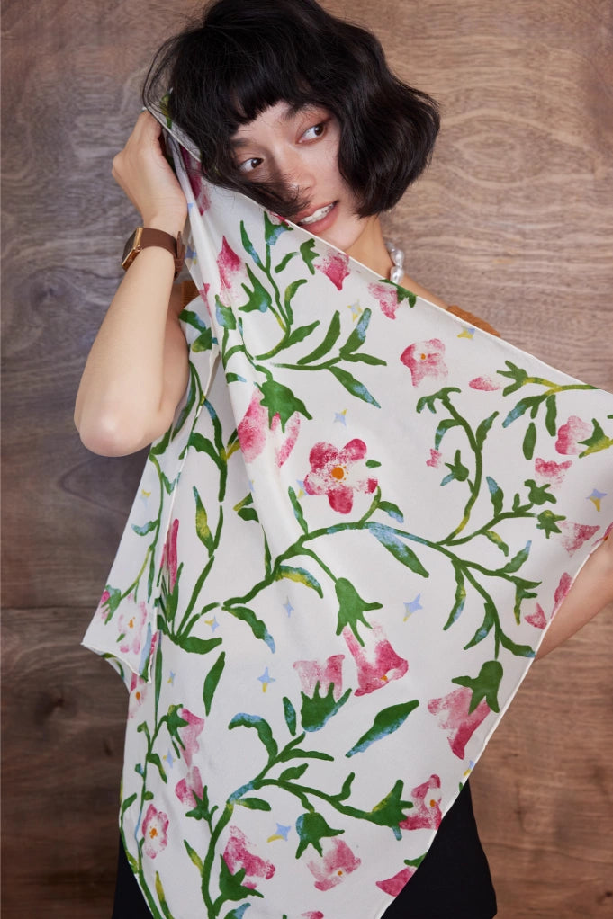 Close-up of a silk square scarf featuring a delicate pink morning glory floral pattern on a white background, highlighting its intricate design.
