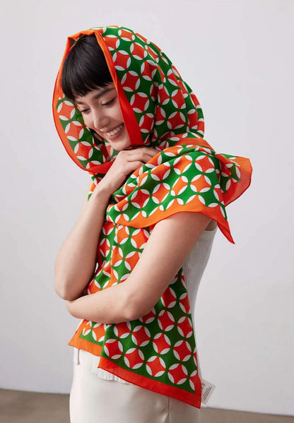 Orange green geometric silk scarf styled as a head scarf and shoulder wrap
