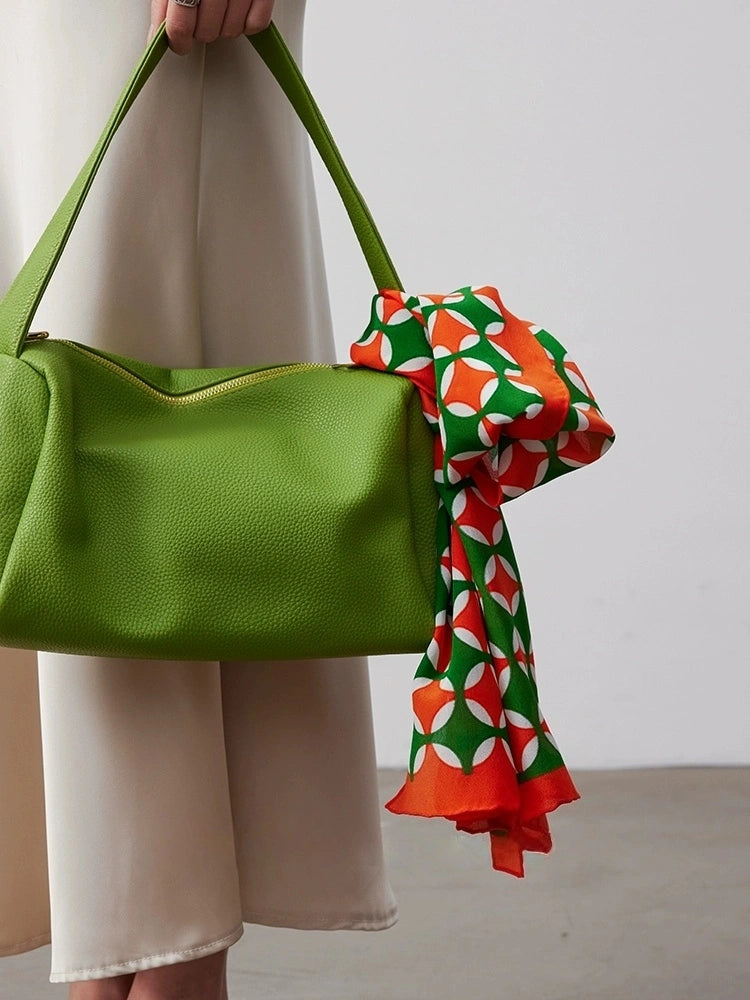 Orange green geometric silk scarf tied to a green handbag as an accessory