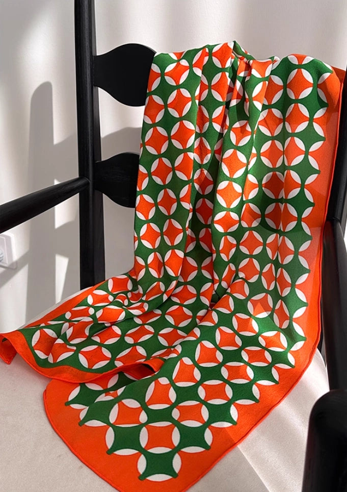 Orange green geometric long silk scarf displayed on a chair to show full pattern and drape