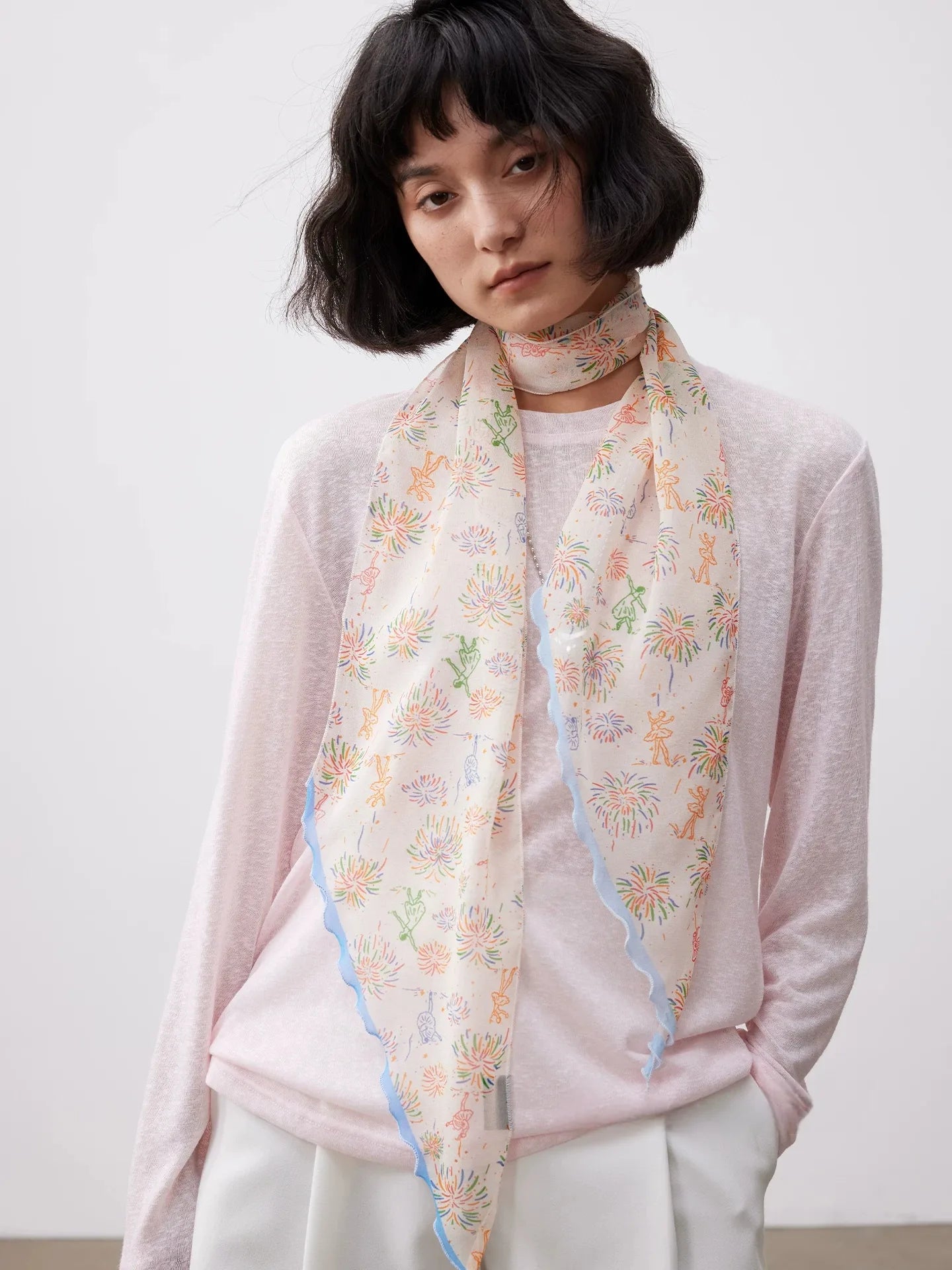 White mulberry silk skinny scarf styled around the neck with a delicate colorful fireworks print