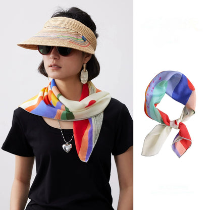 Woman wearing an abstract sunset mountain mulberry silk square scarf styled as a neck scarf with a straw visor